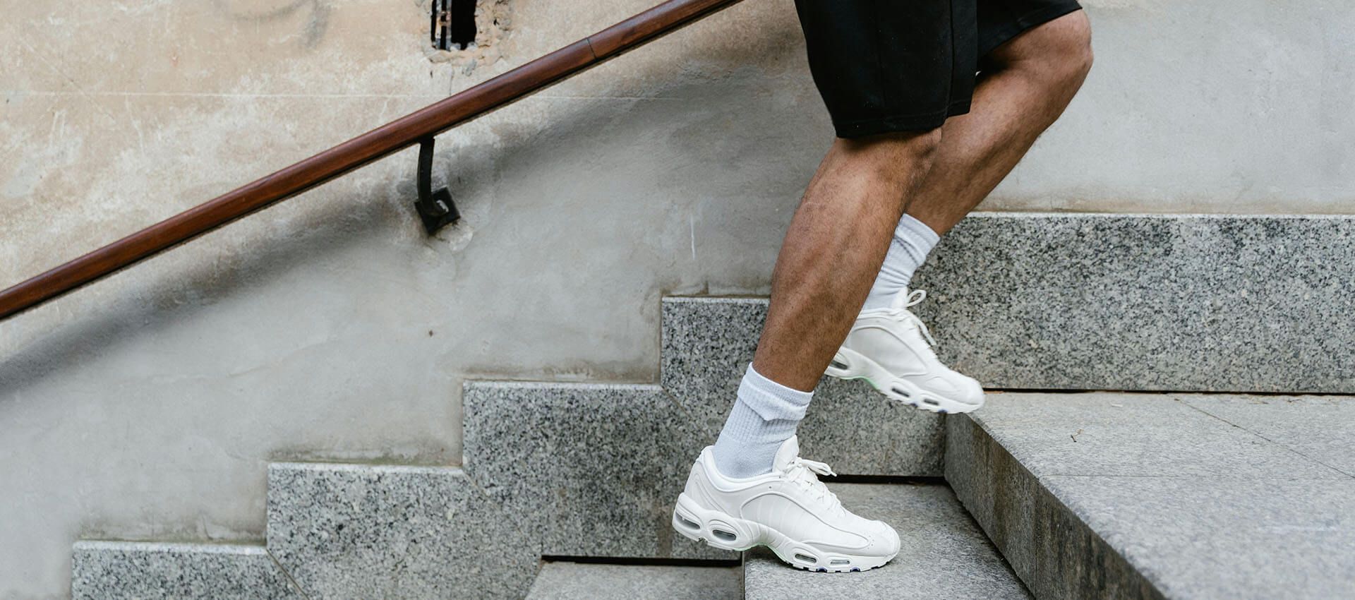 A person wearing white sneakers is walking up a set of stairs.