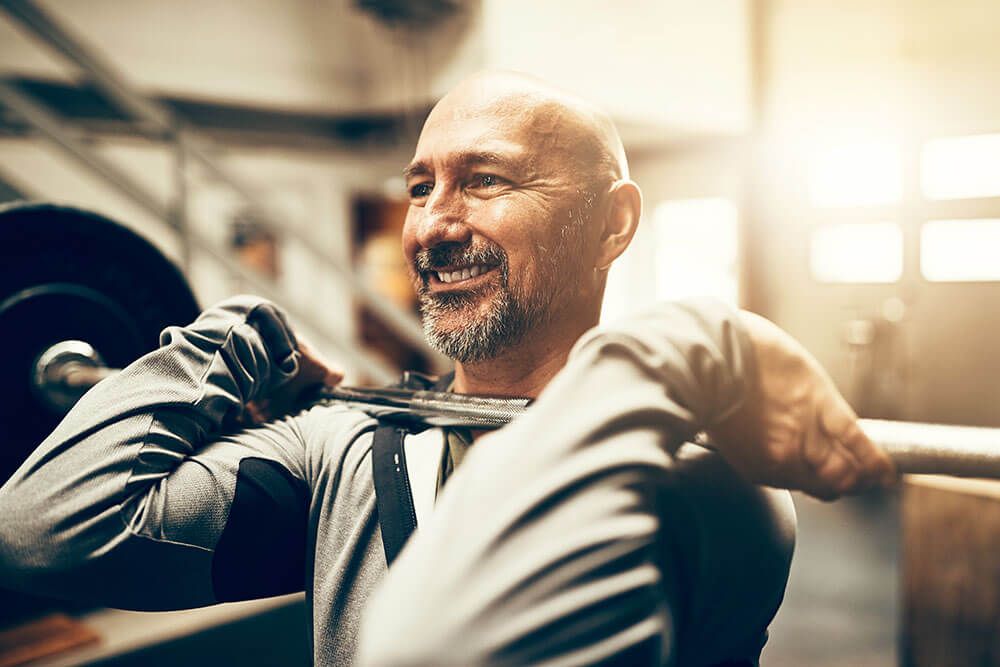A man is lifting a barbell over his head in a gym.
