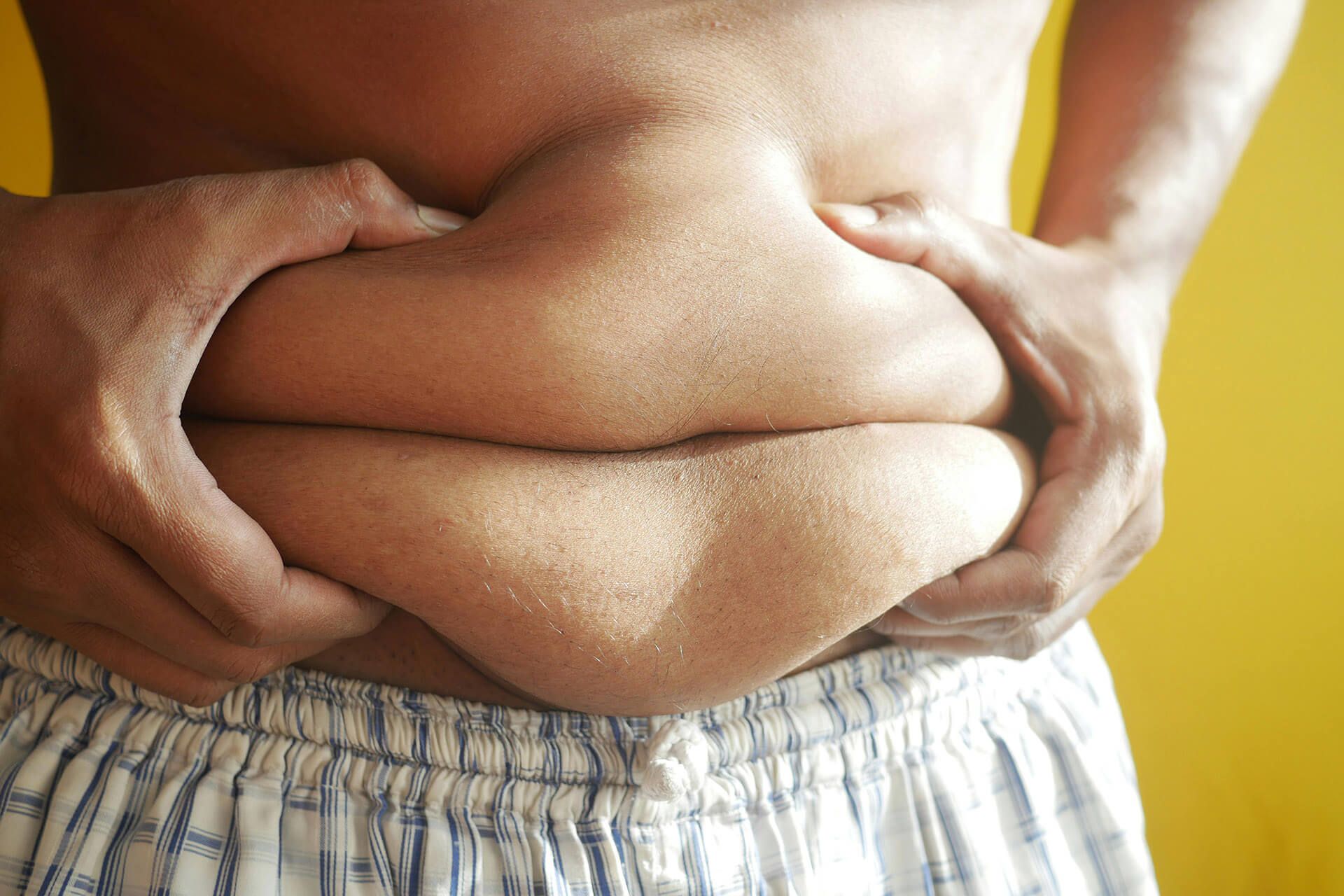 A close-up view of hands holding and pinching excess skin around the midsection.