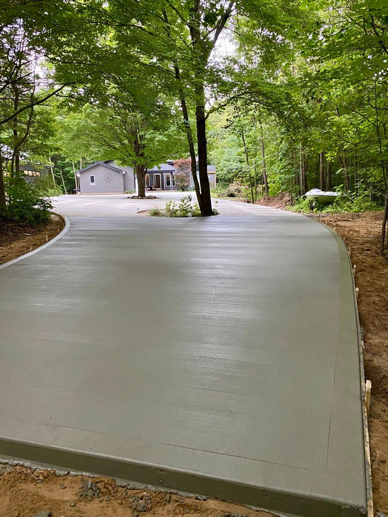 A concrete driveway is being built in the woods next to a house.