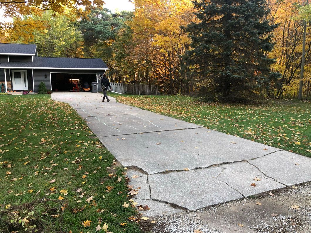 A man is walking down a concrete driveway in front of a house.