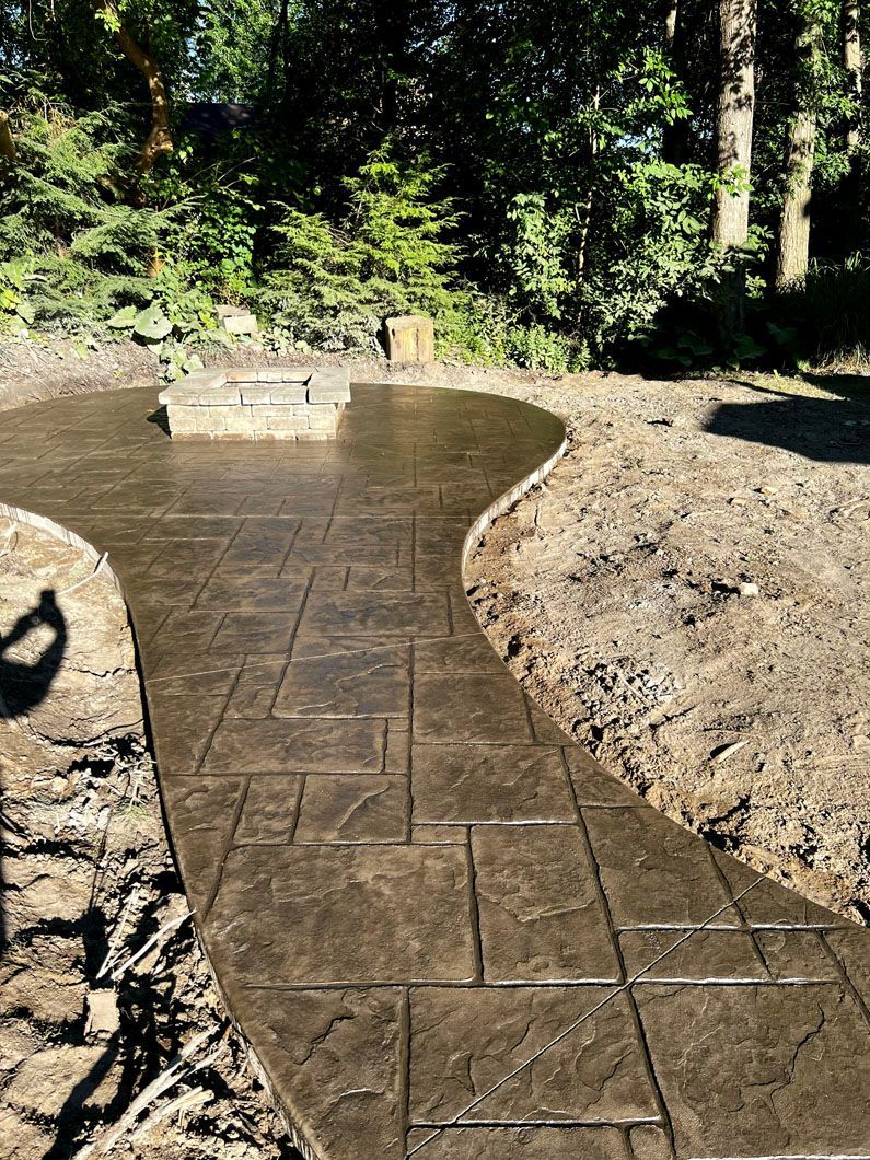 A concrete walkway in a backyard with trees in the background.
