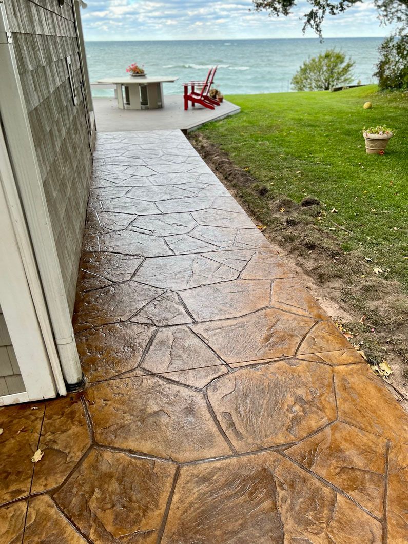 A concrete walkway leading to a patio with a view of the ocean.