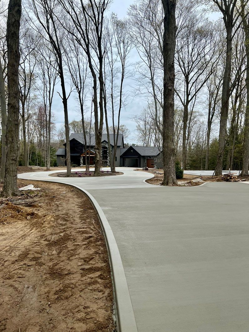 A concrete driveway leading to a house in the woods.