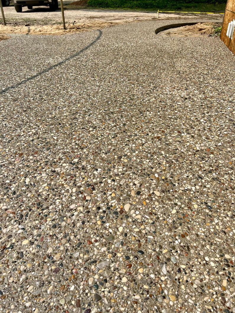 A close up of a gravel driveway with a car parked in the background.