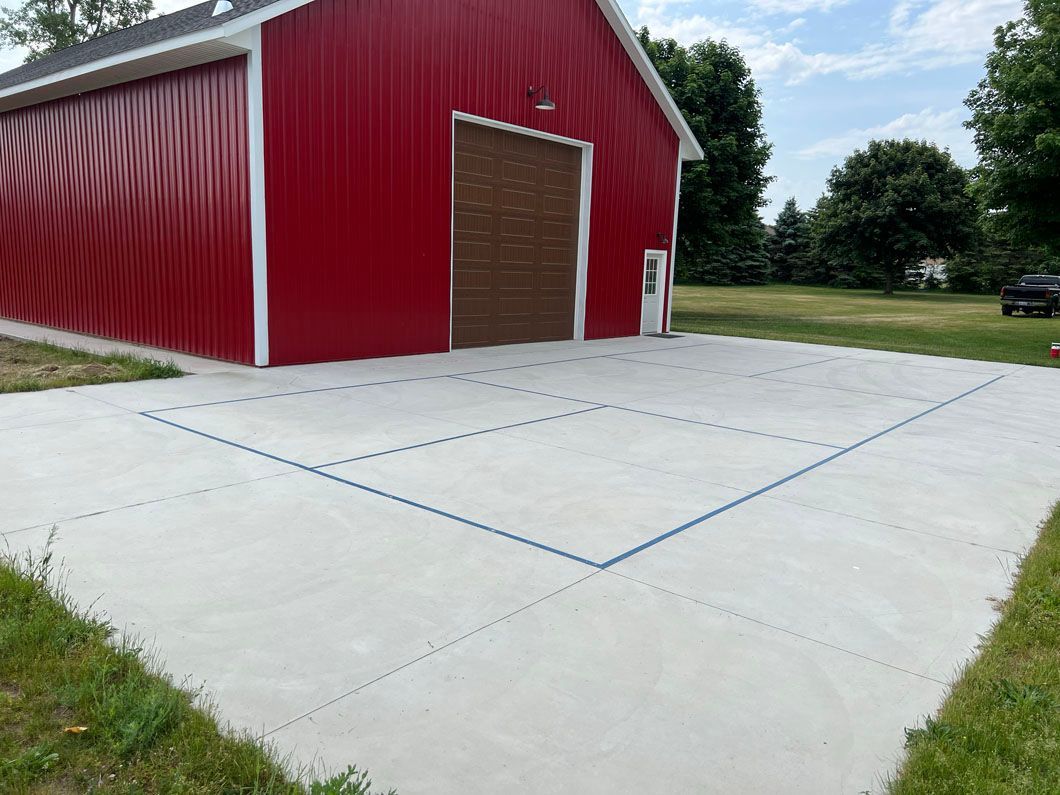 A red barn with a concrete driveway in front of it.