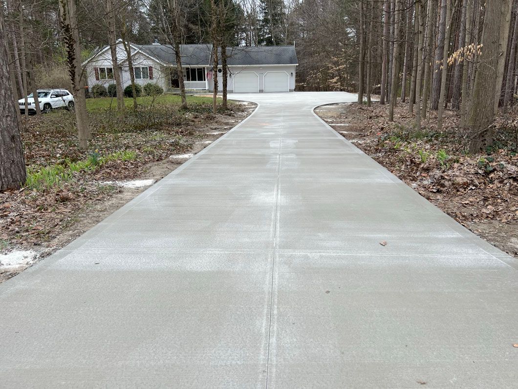 A concrete driveway leading to a house in the woods.