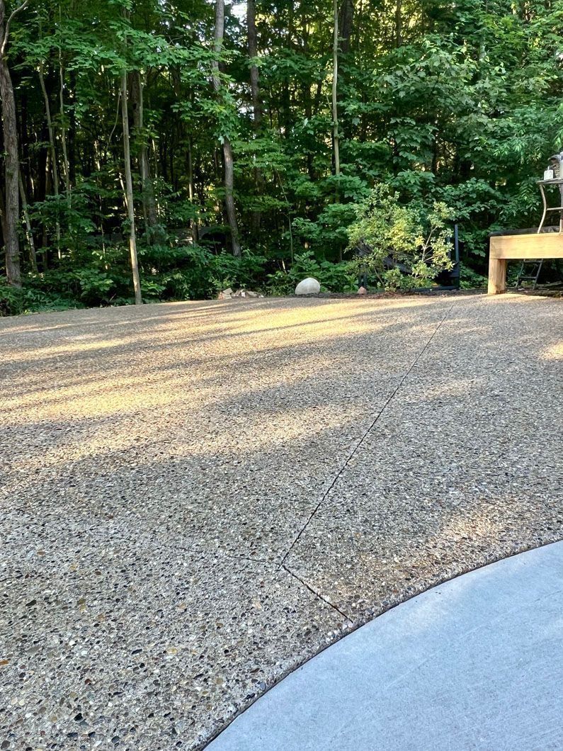 A gravel driveway with a bench in the background and trees in the background.