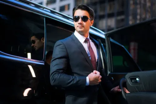 Man in suit and sunglasses exiting a black car in a city setting.
