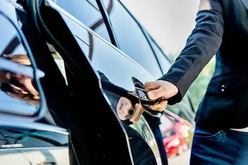 Person in a black suit opening the door of a shiny black car.