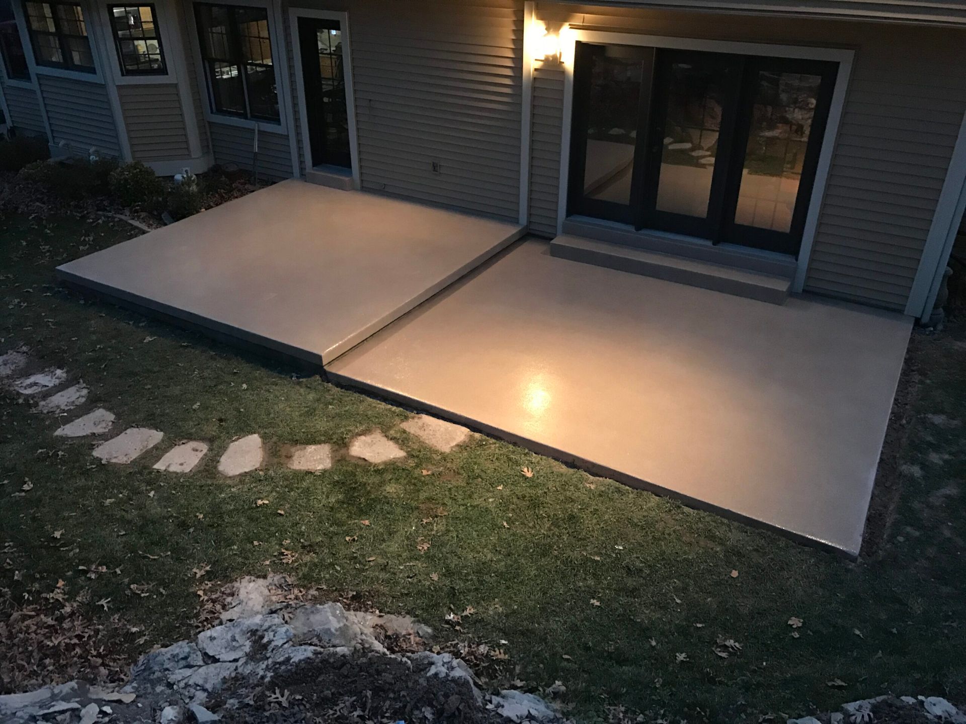 A patio with a walkway leading to it and a house in the background.