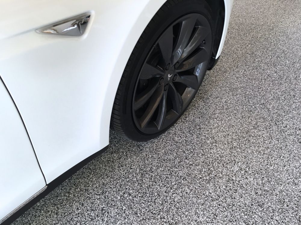 A white car with black wheels is parked in a garage.