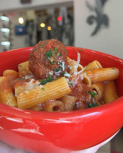 Una persona tiene in mano una ciotola rossa di pasta e polpette