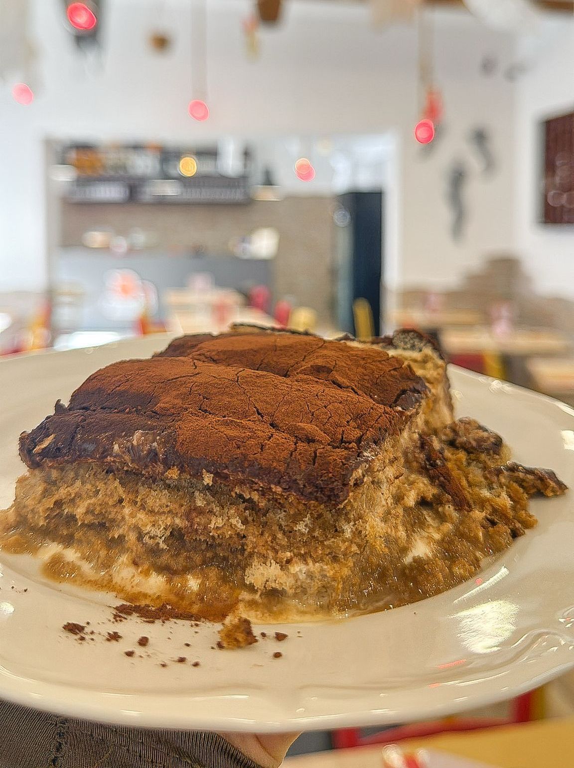 Una persona tiene in mano un piatto bianco con sopra un pezzo di tiramisù.