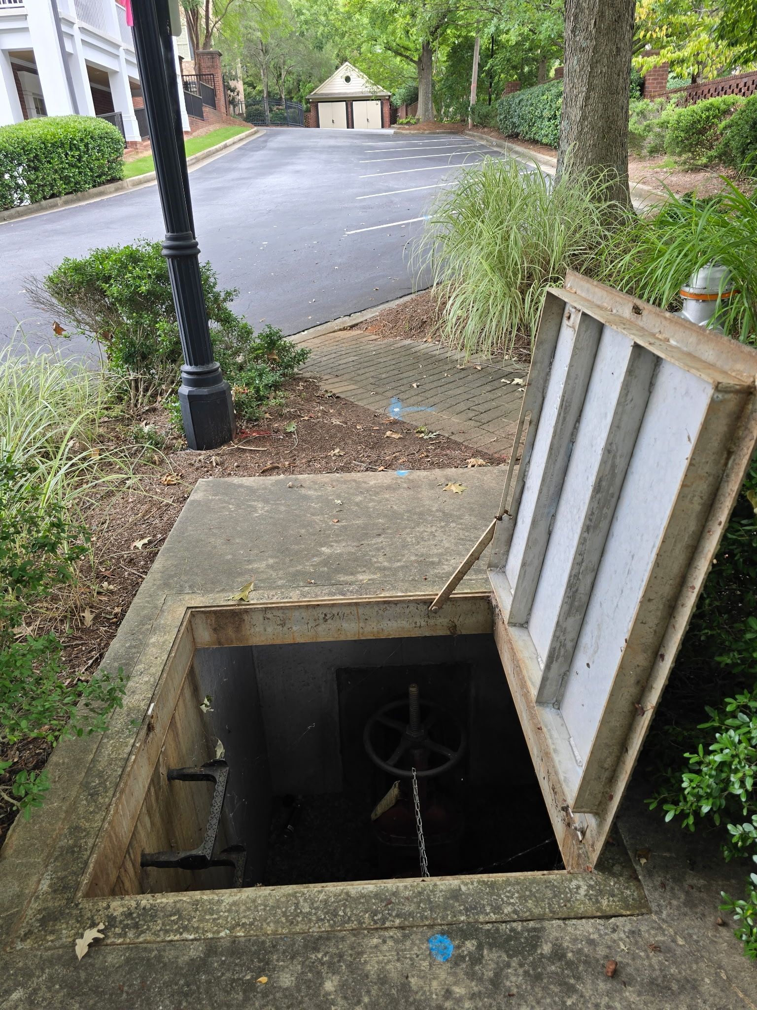 Woman in work clothes inspects pipes under a sink, holding clipboard and wearing gloves.