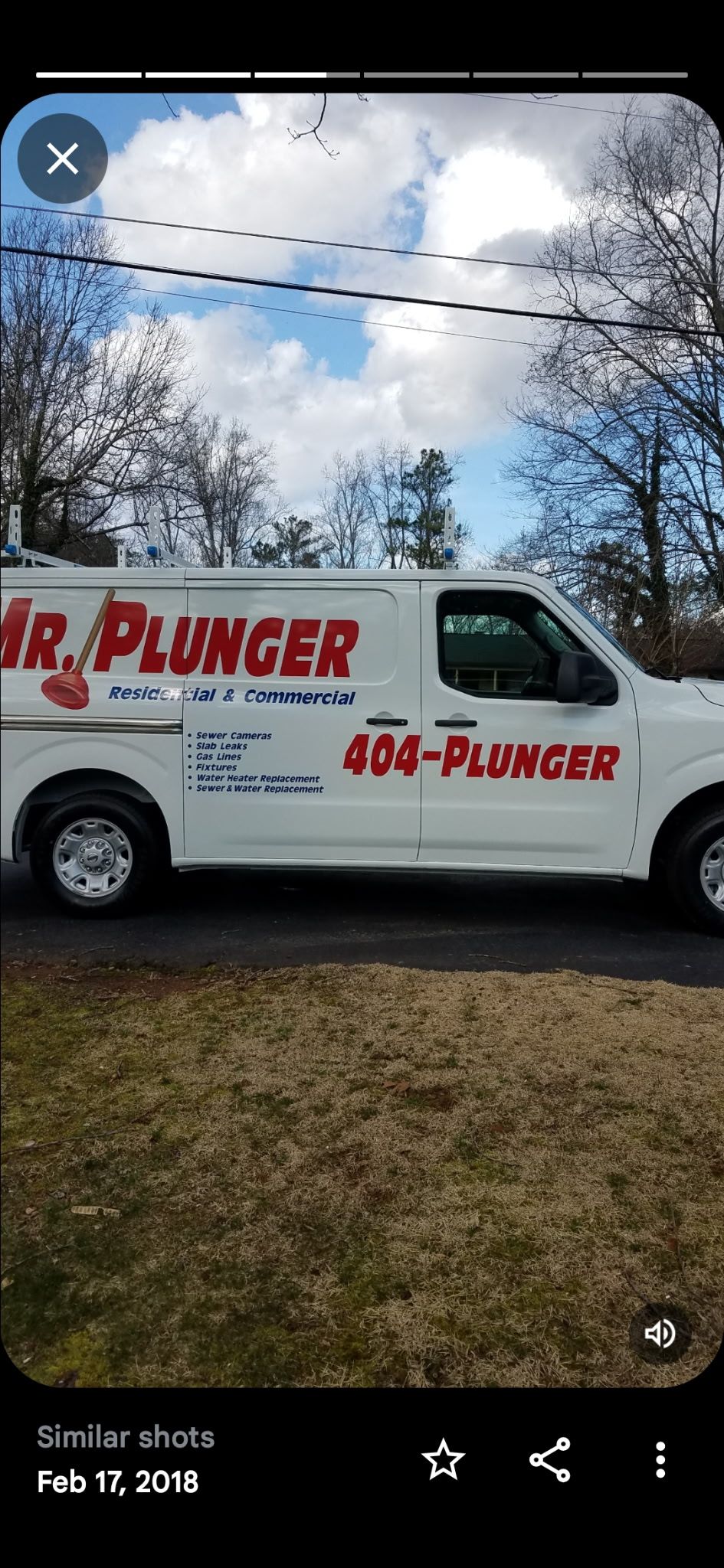 Plumber in overalls and cap repairing a hot water heater with a screwdriver, in a tiled bathroom.