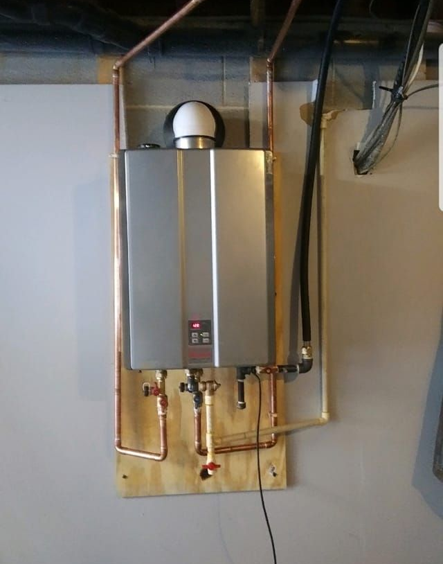 Plumber fixing a water heater on a white wall; uses a wrench and wears gloves.