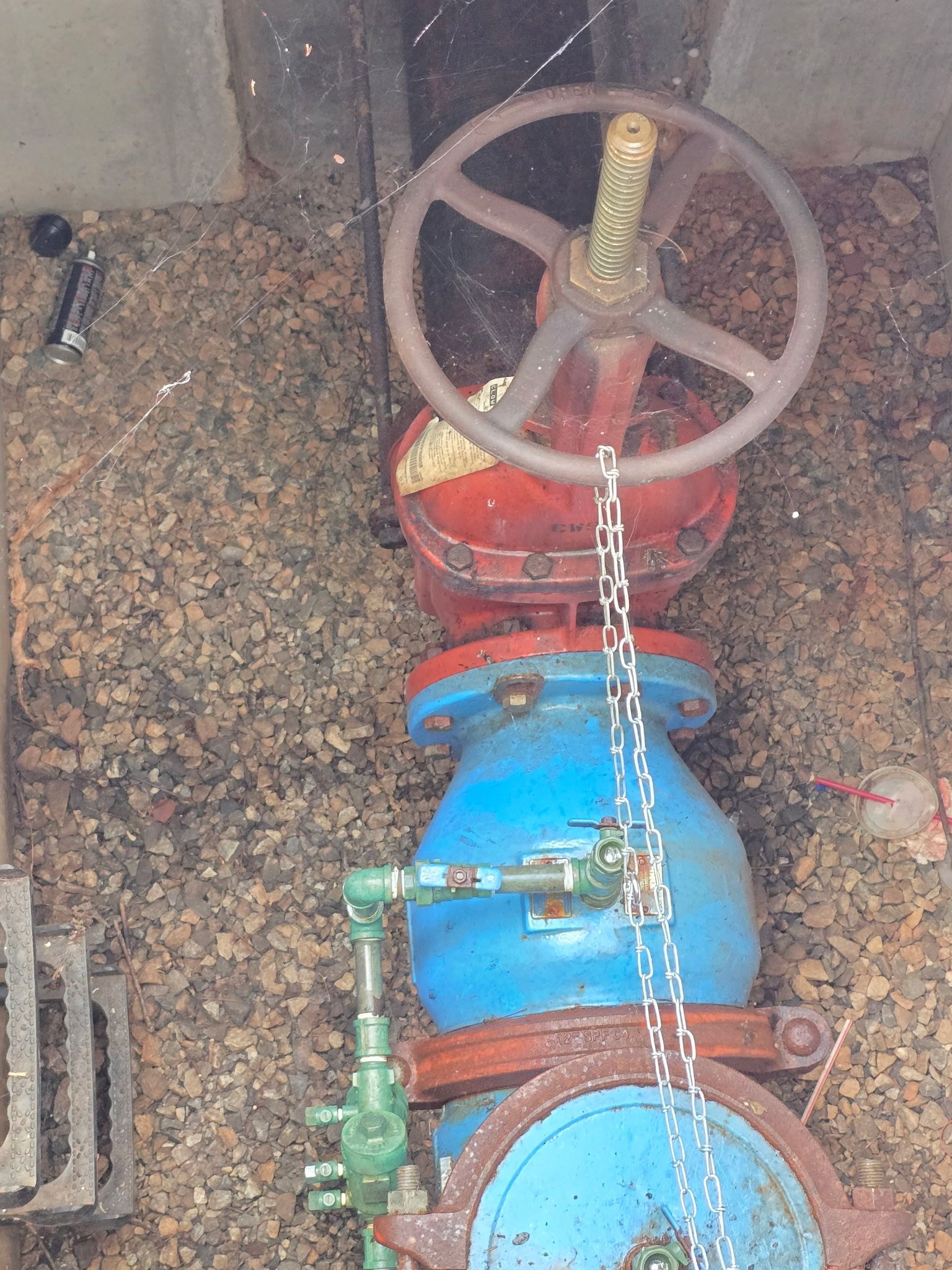 Technician working on boiler, using a screwdriver, wearing a plaid shirt, green gloves, and cap.