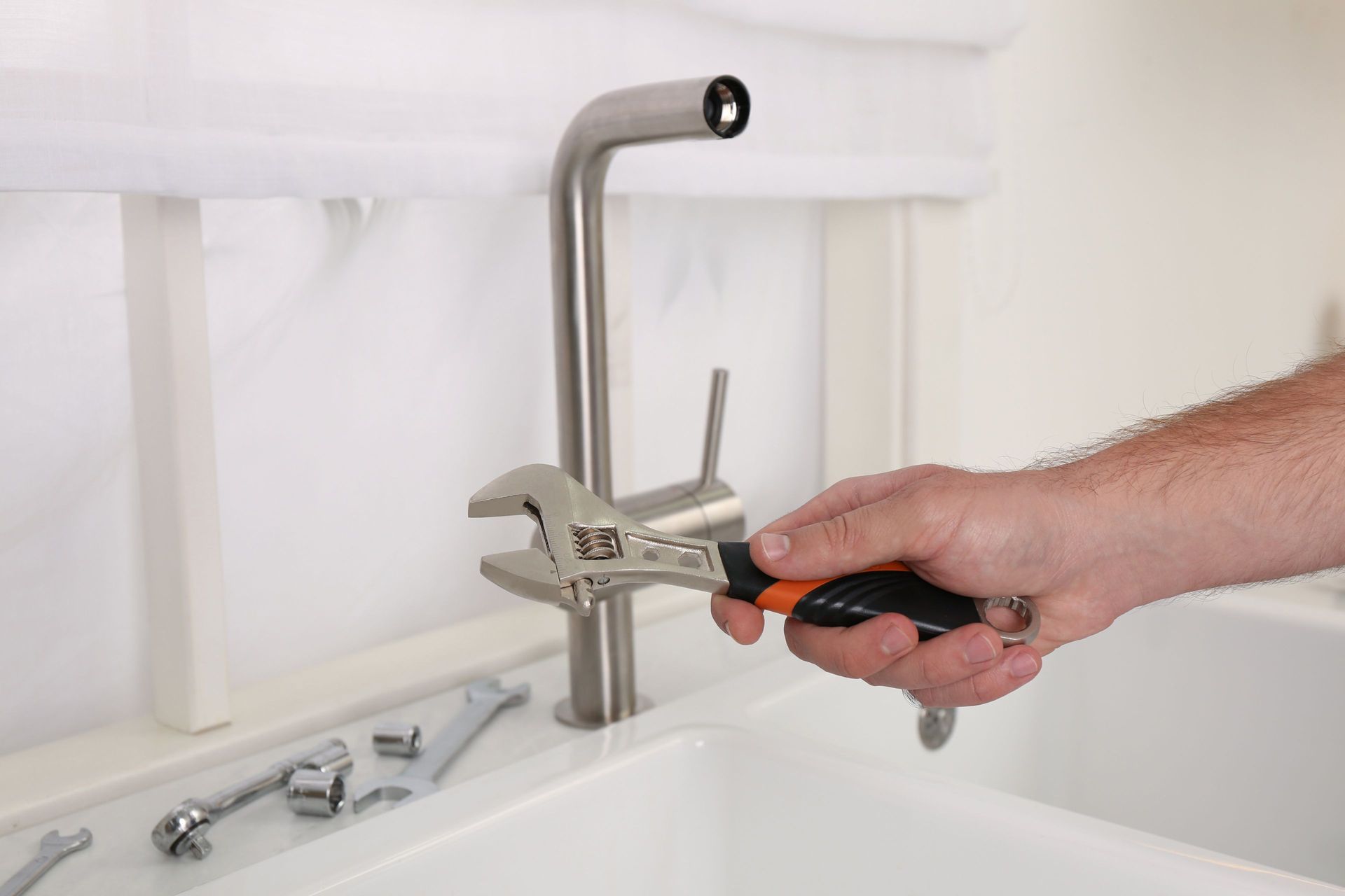 A person's hand using a wrench to tighten a faucet in a white sink. A person's hand using a wrench to tighten a faucet in a white sink.