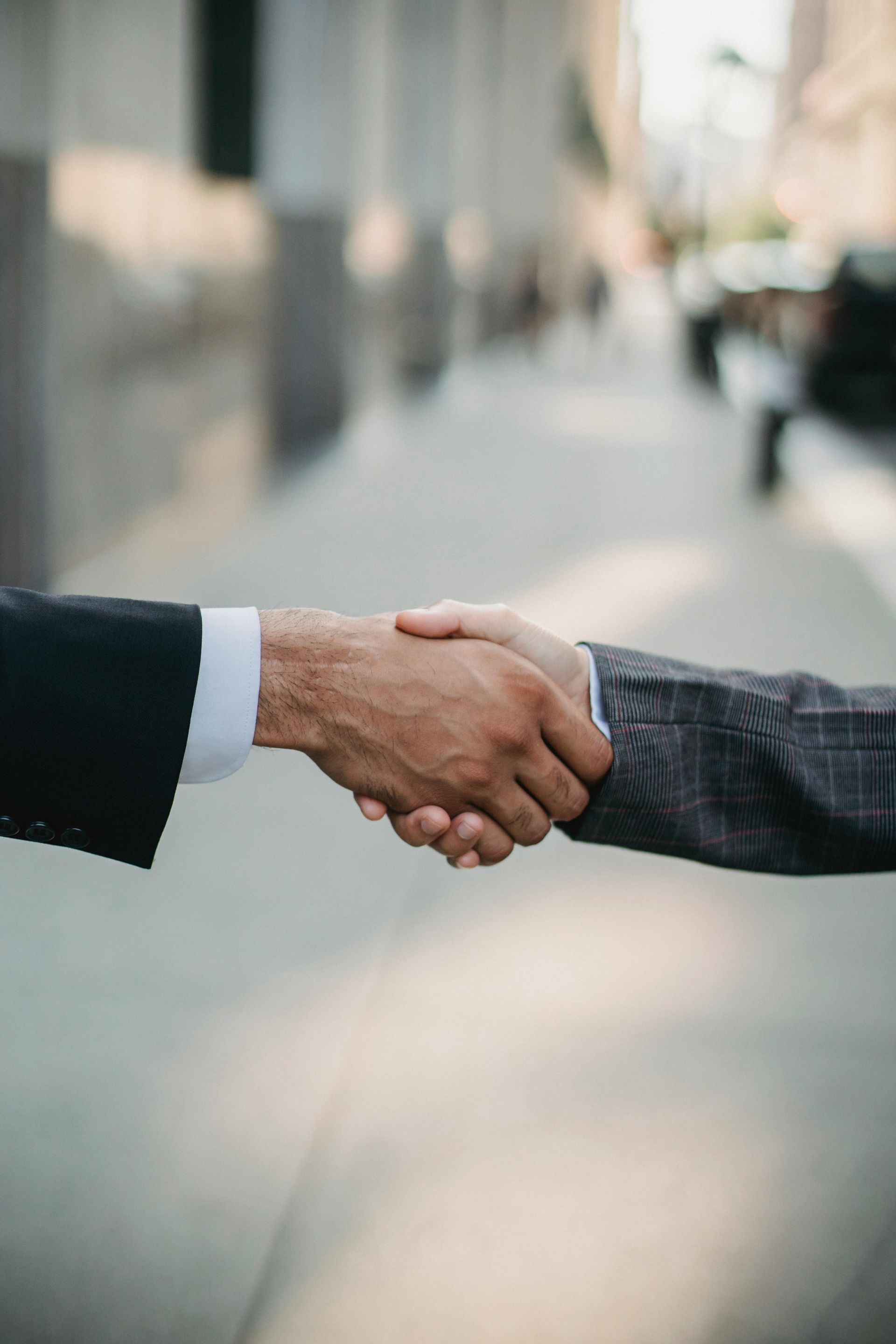 Two men in suits are shaking hands on a sidewalk.