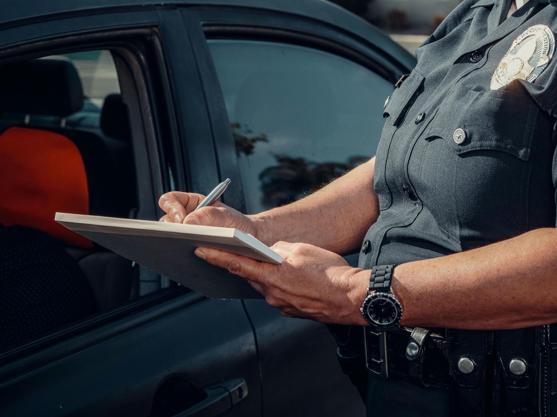 A police officer is writing on a clipboard in front of a car.