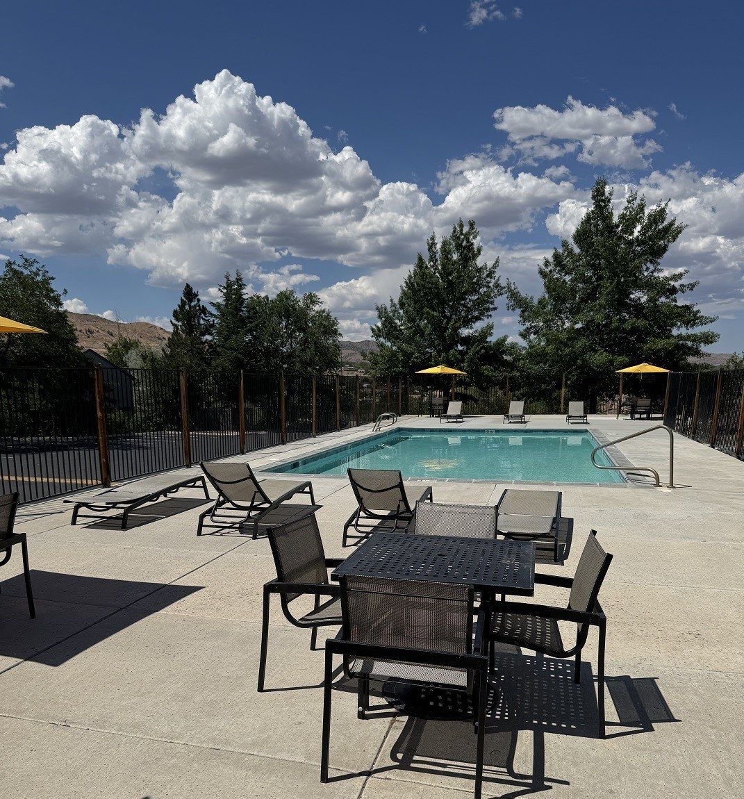 Pool area with lounge chairs, tables, and umbrellas under a cloudy sky.