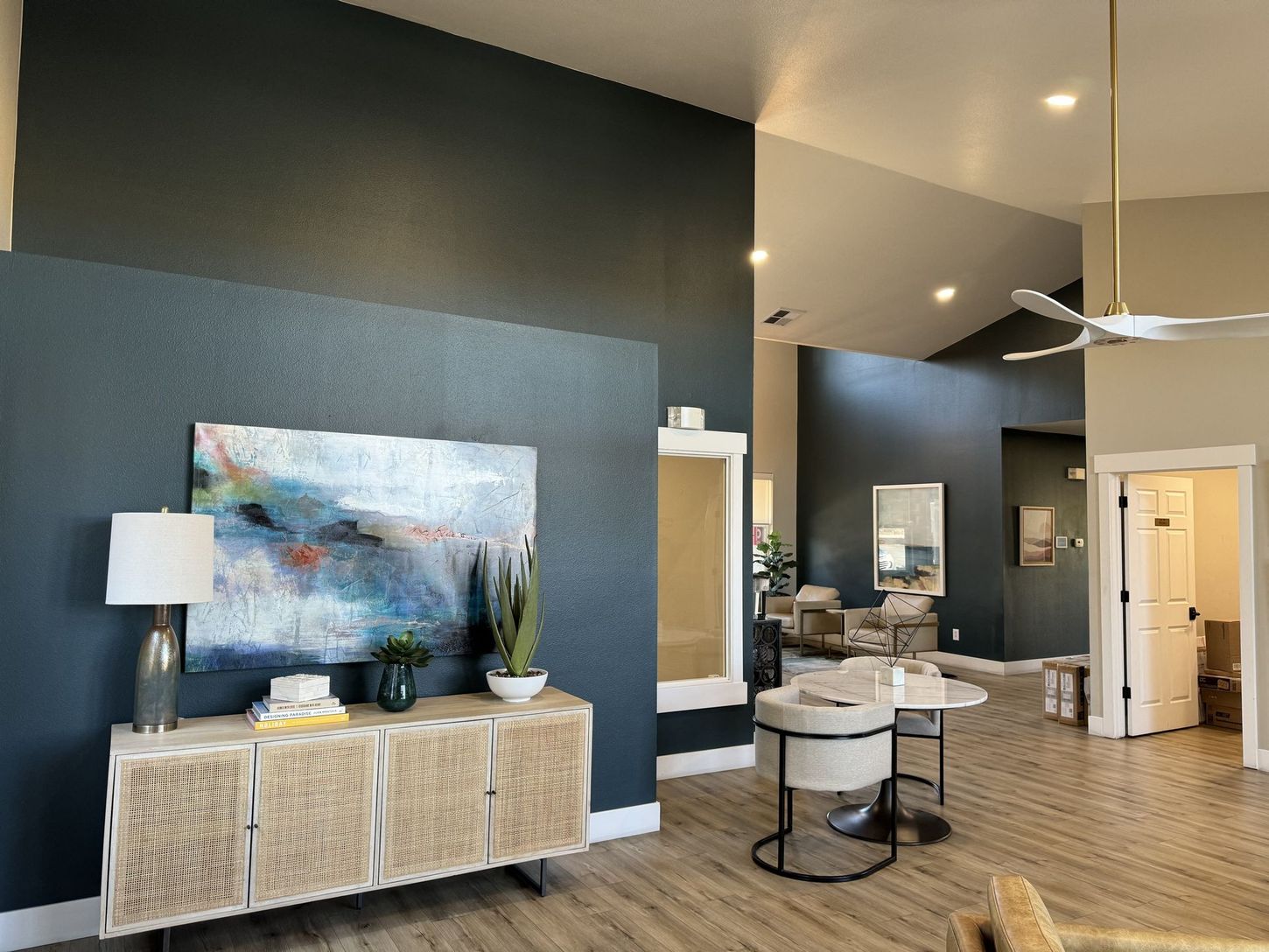 A modern interior with teal walls, a woven cabinet, artwork, and a table with chairs.
