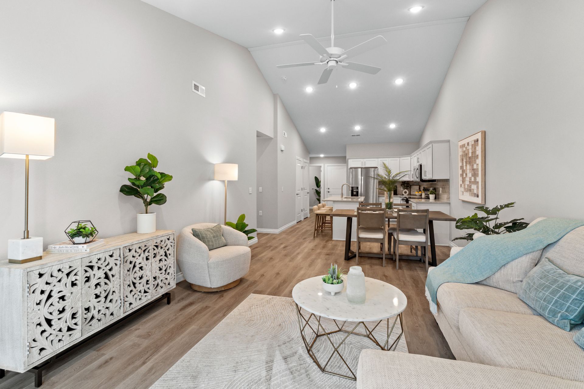 Photo of a room with a high, angled ceiling, showing a dining area in the middle ground and a kitchen in the background
