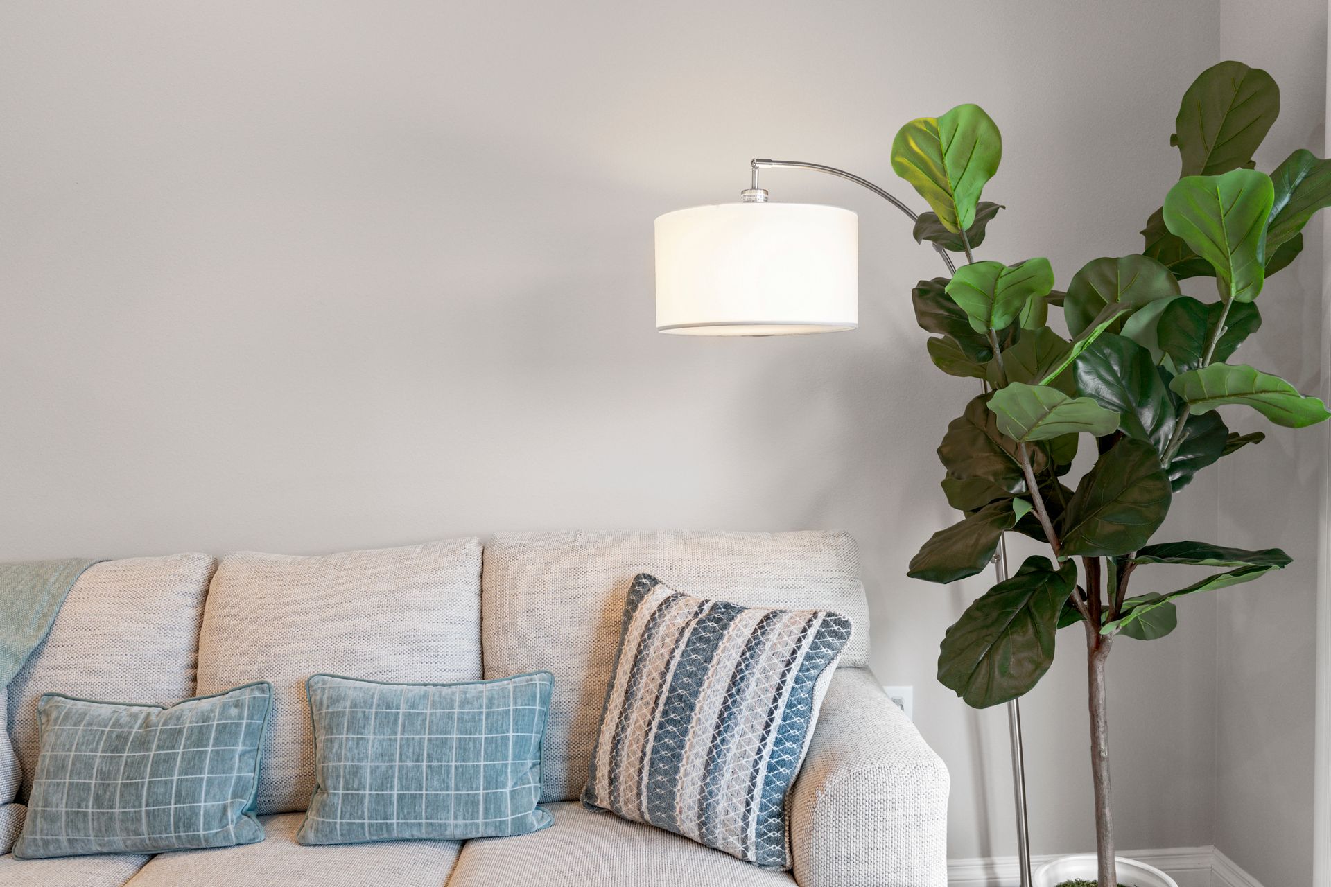 Close up photo of a couch, with a lamp and a fake plant next to it