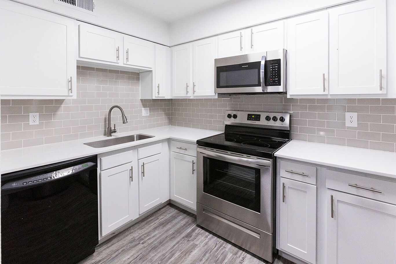White kitchen with stainless steel appliances and black dishwasher.