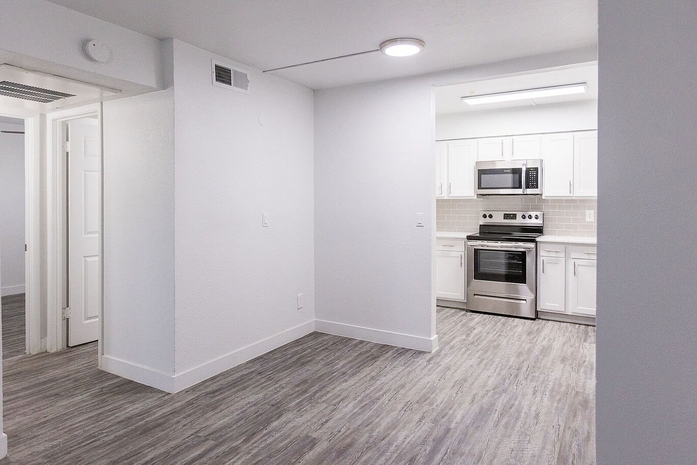 Empty apartment with gray flooring, white walls, and a kitchen with stainless steel appliances.