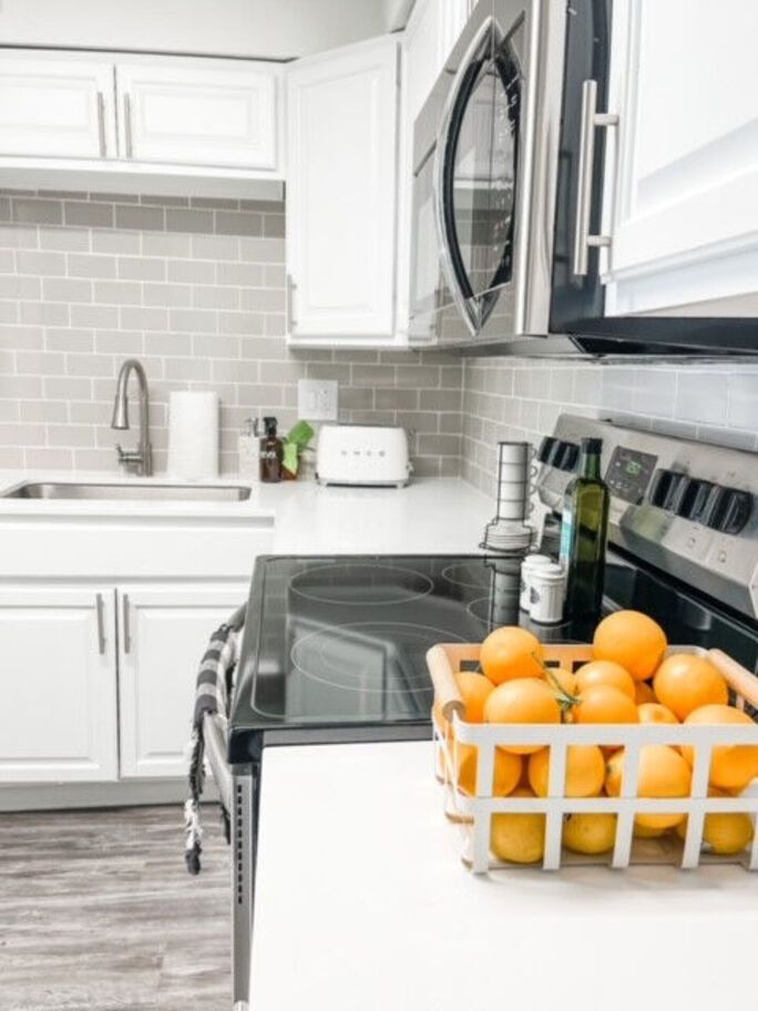 White kitchen with grey tile backsplash, stainless steel appliances, and a basket of oranges.