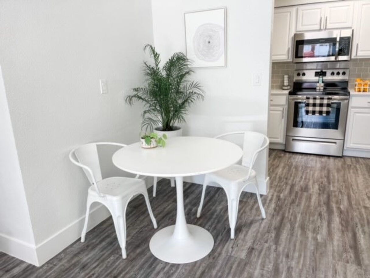 White table with two chairs, plant, and kitchen in a bright, modern space.