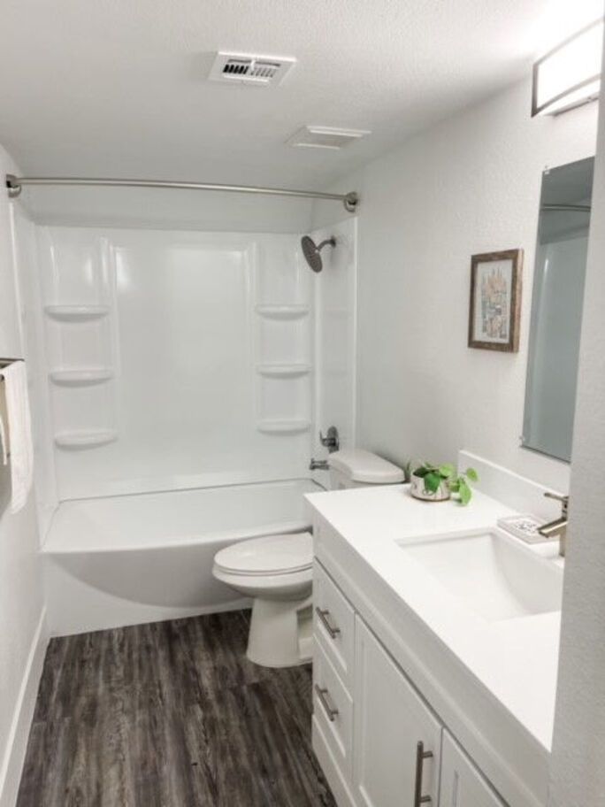 Bathroom with a white tub and vanity, gray wood-look floor, and a small picture on the wall.