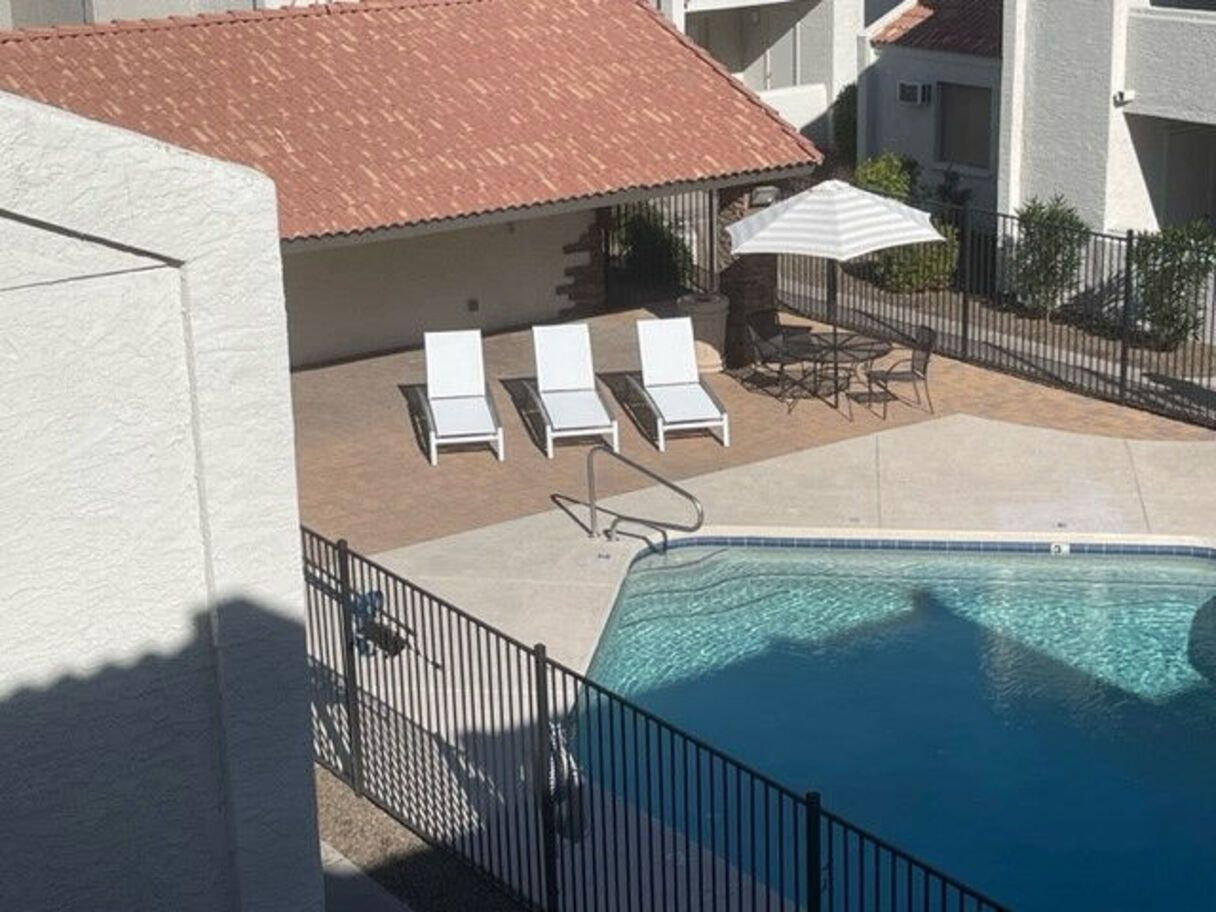 Pool area with lounge chairs, table, umbrella, and pool.