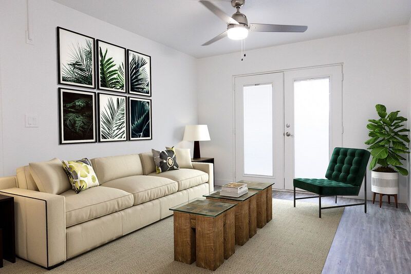 Living room with white walls, tan sofa, framed botanical prints, green chair, and French doors.