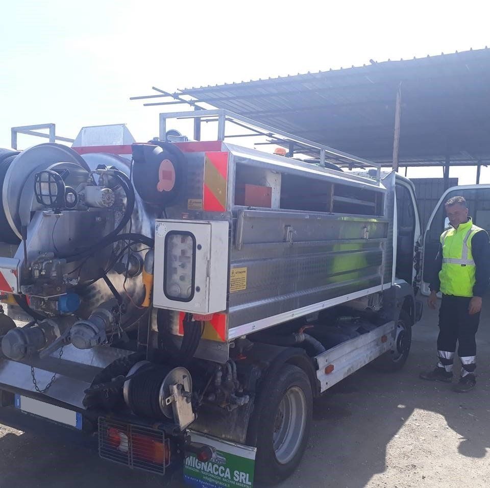 Un operaio è in piedi accanto a un camion per la pulizia delle strade. Il camion è argentato e dotato di vari tubi e attrezzature.