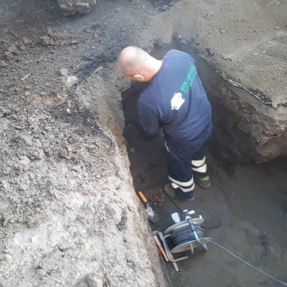 Uomo con camicia blu che lavora in una trincea; sono visibili una bobina di filo e degli attrezzi.
