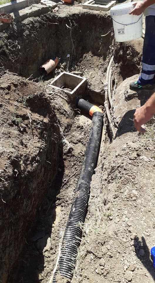 Cantiere: tubo corrugato in una trincea, collegato a una scatola quadrata. Persona che versa liquido da un secchio bianco.
