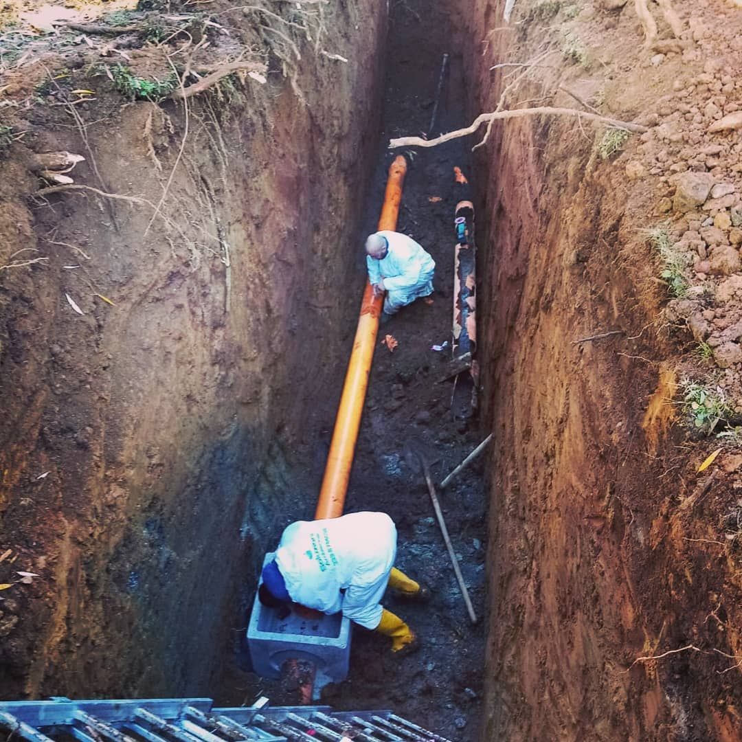Operai in tute protettive installano tubi in una trincea profonda.