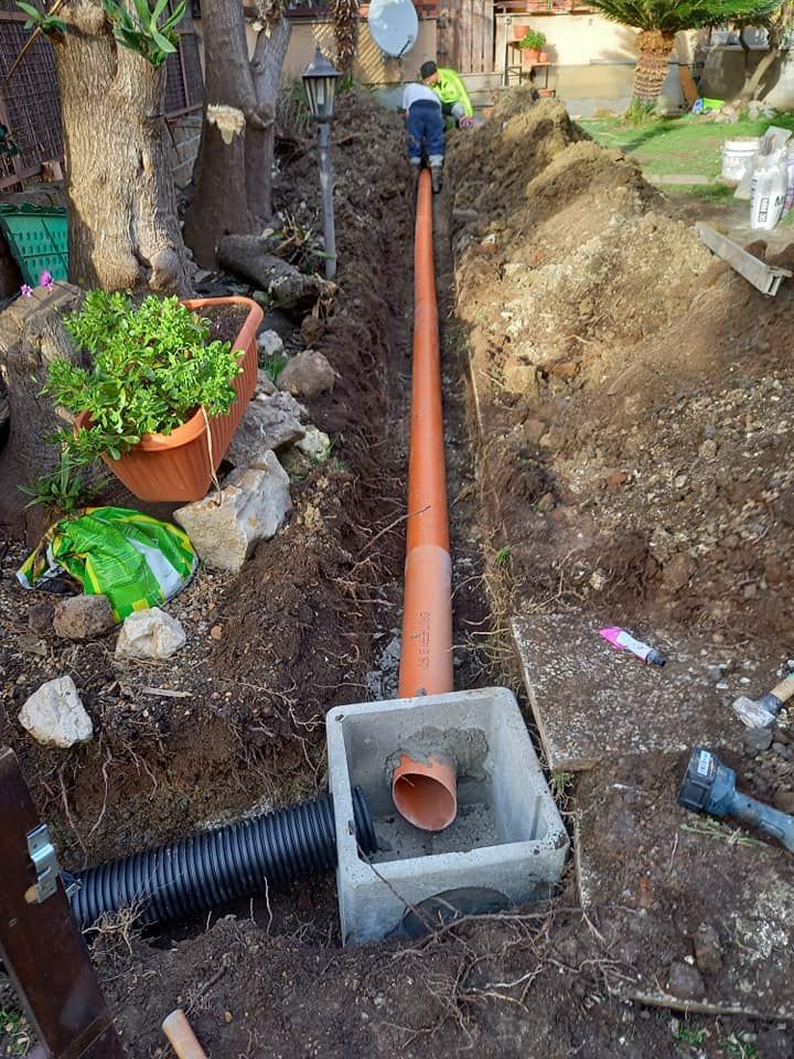 Una persona che installa un sistema di drenaggio in un giardino, con tubi arancioni e neri visibili.