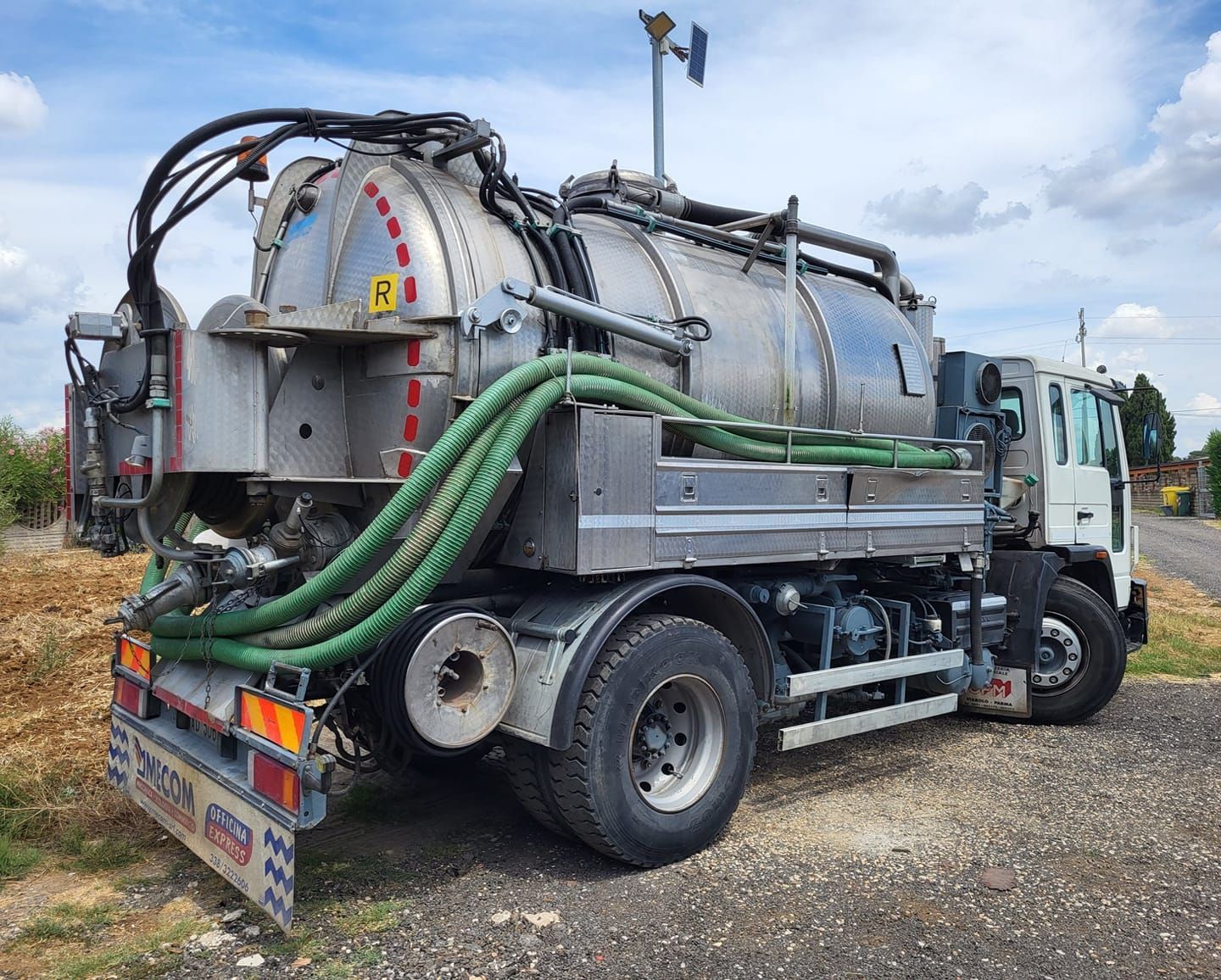 Autocisterna con un grande serbatoio argentato e tubi verdi parcheggiata all'aperto.
