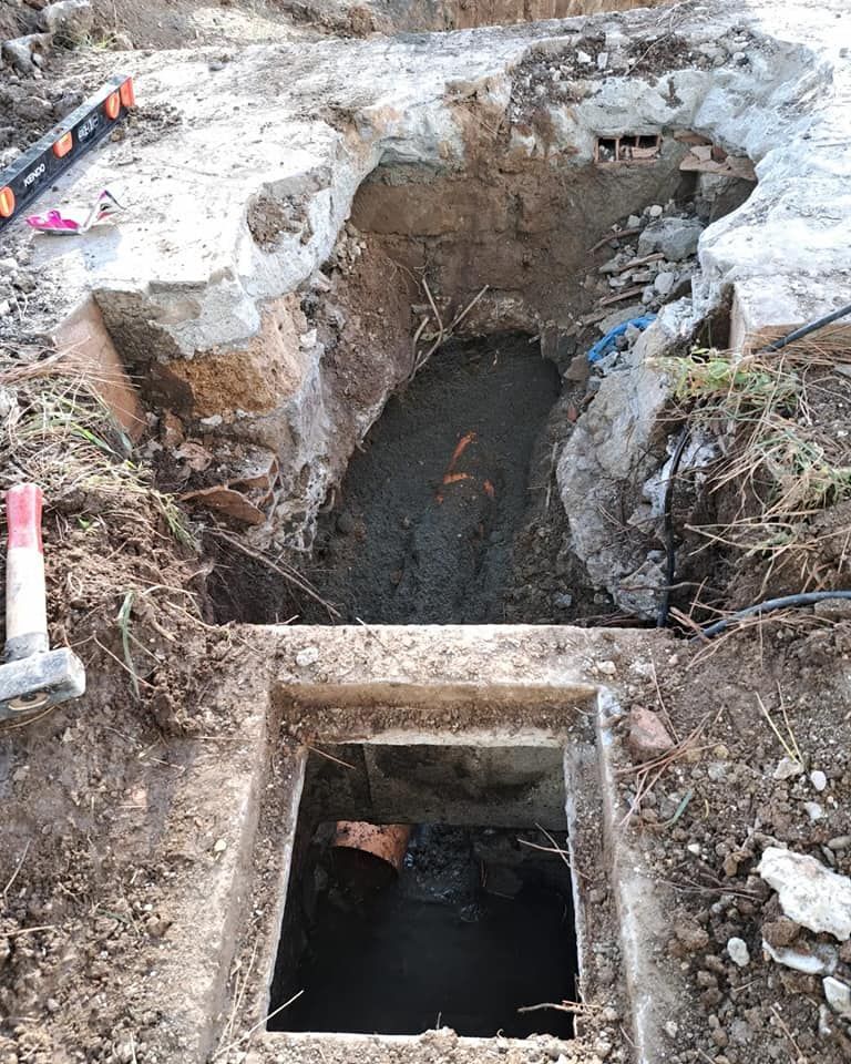 Area scavata con una struttura in cemento, che ha portato alla luce tubature sotterranee, terreno e detriti.