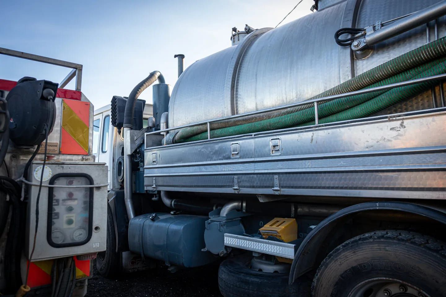 Autocisterna settica, cisterna argentata, tubo verde, parcheggiata all'aperto.