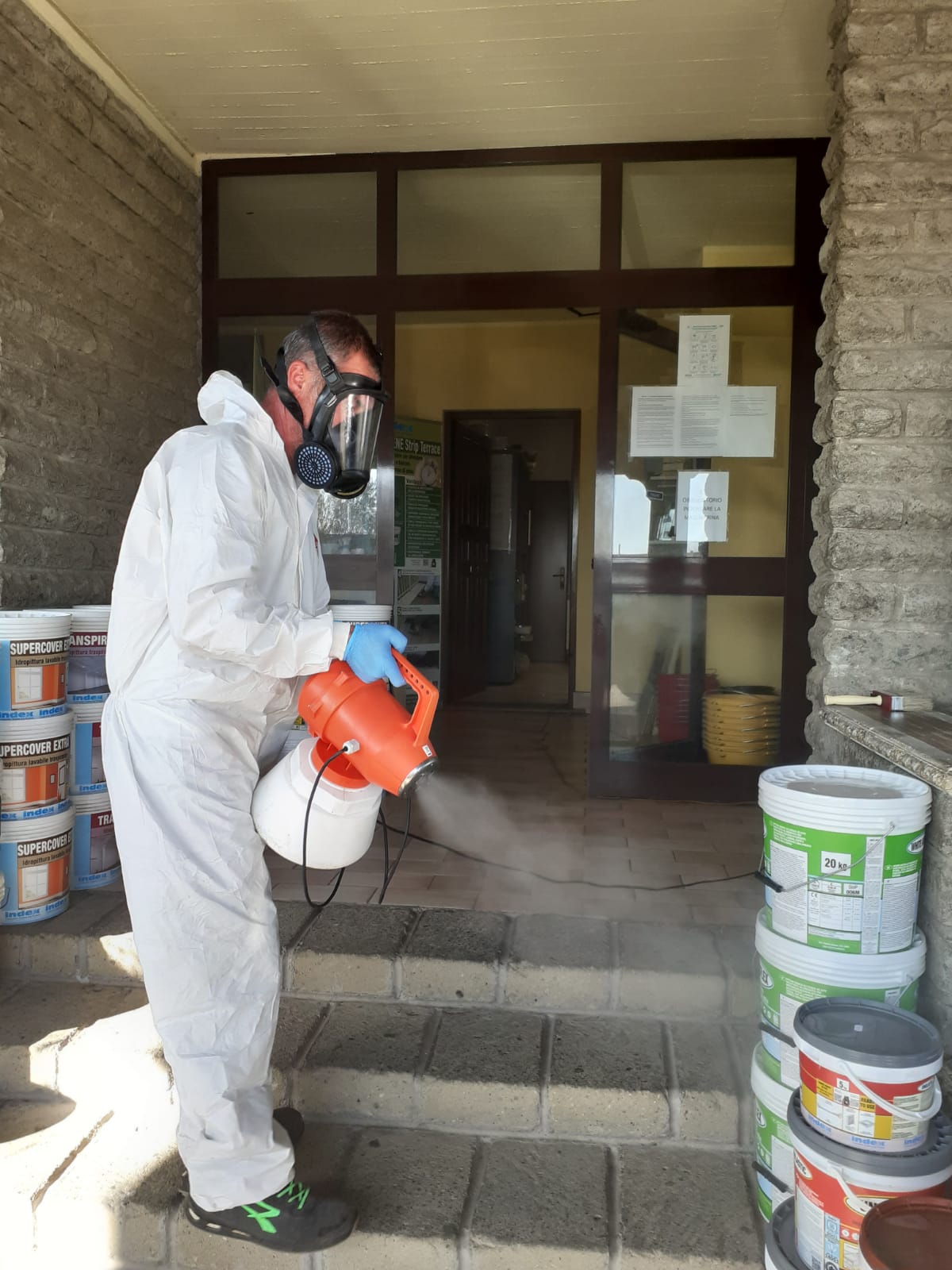 Persona con tuta protettiva che spruzza disinfettante all'ingresso dell'edificio.