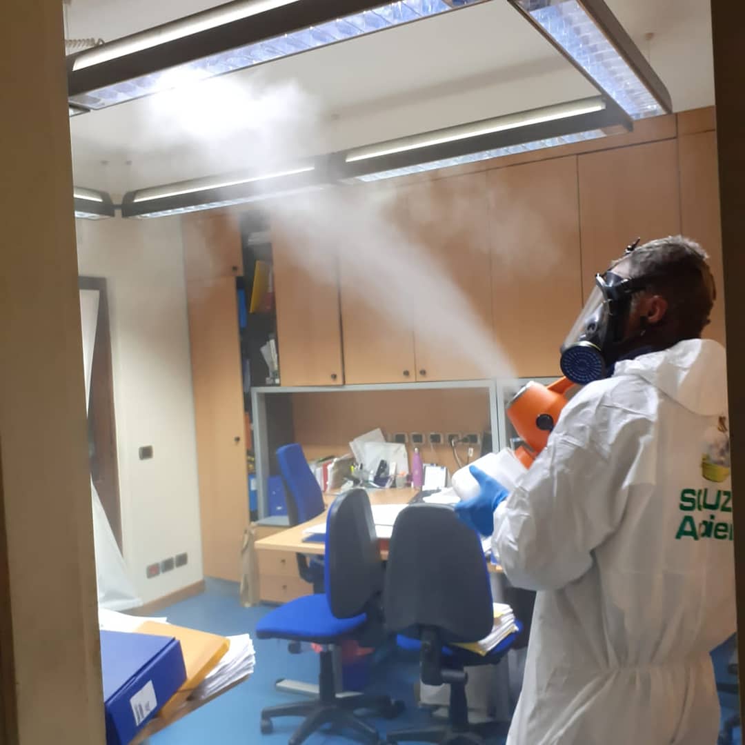 Persona con tuta protettiva che disinfetta un ufficio utilizzando uno spruzzatore.