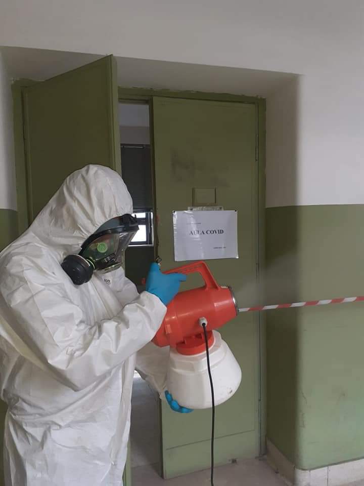 Persona con tuta protettiva che disinfetta una stanza con uno spruzzatore.