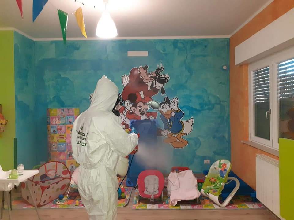 Persona in tuta protettiva che disinfetta una sala giochi per bambini con un murale di Topolino.