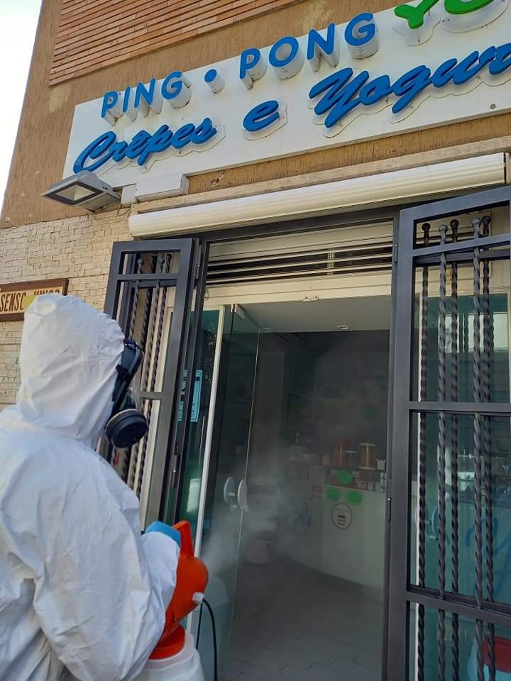 Persona in tuta protettiva che disinfetta l'ingresso di un negozio: negozio