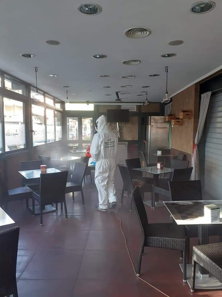 Persona con tuta protettiva che disinfetta un bar con uno spruzzatore.